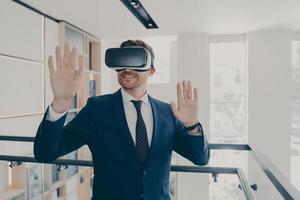 Smiling office worker in vr headset touching air and gesturing while working in virtual reality photo