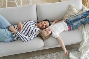 Little daughter and mother lying on sofa relax, have lazy weekend together. Happy motherhood photo