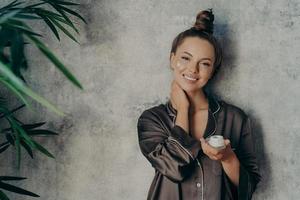 Beautiful caucasian woman in silk pajama with face cream smiling at camera photo