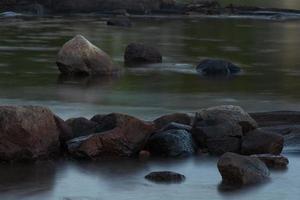 A long exposure image of water flowing around rock. photo