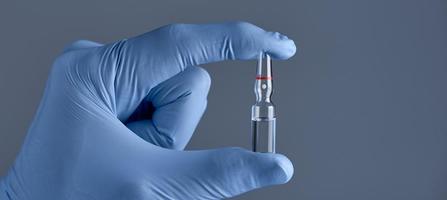 Hand in medical blue glove holding ampoule on a grey background. Concept of medical help. photo