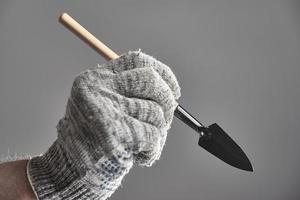 Hand in old glove holding gardening spade like a pen on gray background. The concept of gardening. photo