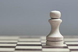 un primer plano de un peón blanco en un tablero de ajedrez sobre un fondo gris. foto con espacio de copia.