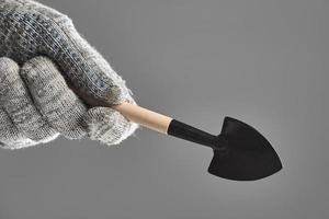 Gardening spade or trowel in human hand with protective gloves isolated on gray background.