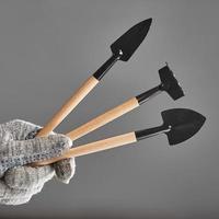 Hand in old glove holding gardening tools isolated on gray background. photo