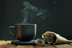 Photo with copy space. Cup of hot tea with steam and a bag of tea bags on the wooden table over black background.