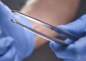 A gloved hand holding tweezers against gray background. photo