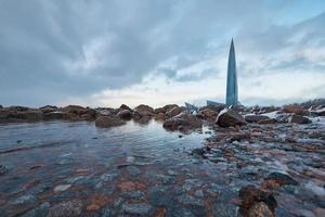 Lakhta center on a background of cloudy sky and large stones covered with frost and ice. photo