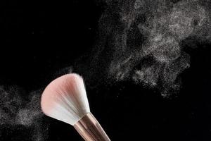 Make-up brush with powder on it and heap of powder on black background. Photo with copy space.