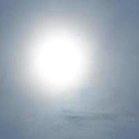 A large solar disk shines through the clouds. Blue and white background. photo