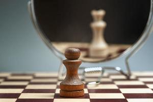 Black pawn on the background of a mirror in which the white Queen is reflected. photo