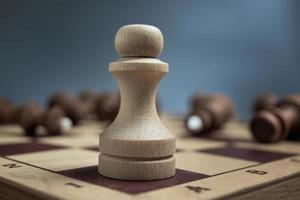 White pawn on the blur background of lying black chess pieces. The concept of one against all. photo