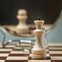 White Queen on the background of a mirror in which the white pawn is reflected. Background in blur. photo