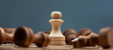 White pawn on the blur background of lying black chess pieces. The concept of one against all. photo