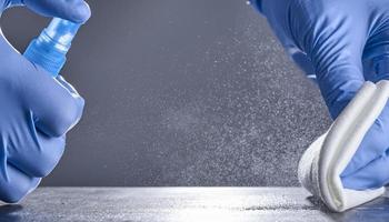 Hands in rubber gloves wipe the table with a disinfectant spray on a grey background. Disinfection of premises photo