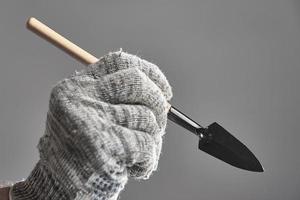 Hand in glove holding gardening spade like a pen on gray background. photo