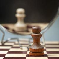 Black pawn on the background of a mirror in which the white pawn is reflected. Background in blur. photo