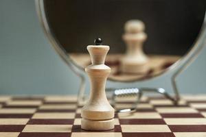 White Queen on the background of a mirror in which the white pawn is reflected. Background in blur. photo