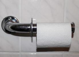 A white roll of soft toilet paper neatly hanging on a modern chrome holder on a light bathroom wall photo