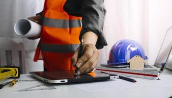 Two colleagues discussing data working and tablet, laptop with on on architectural project at construction site at desk in office photo