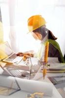 Two colleagues discussing data working and tablet, laptop with on on architectural project at construction site at desk in office photo