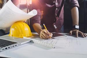 Two colleagues discussing data working and tablet, laptop with on on architectural project at construction site at desk in office photo