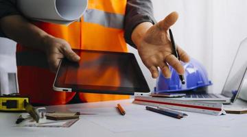 Two colleagues discussing data working and tablet, laptop with on on architectural project at construction site at desk in office photo