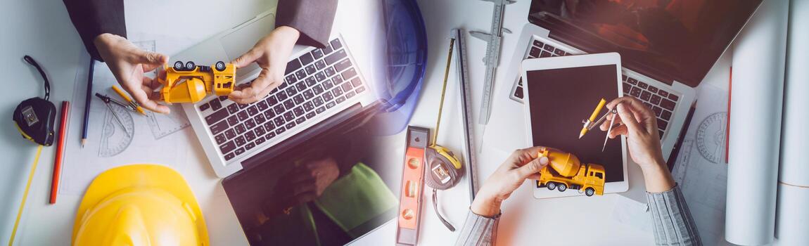 Two colleagues discussing data working and tablet, laptop with on on architectural project at construction site at desk in office photo