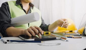 Dos colegas discutiendo el trabajo de datos y una tableta, un portátil con un proyecto arquitectónico en el sitio de construcción en un escritorio en la oficina foto