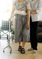 young asian physical therapist working with old man on working using a walker in hallway of nursing home photo