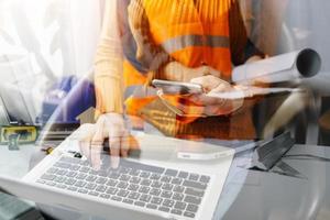 Two colleagues discussing data working and tablet, laptop with on on architectural project at construction site at desk in office photo