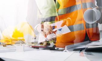 Two colleagues discussing data working and tablet, laptop with on on architectural project at construction site at desk in office photo