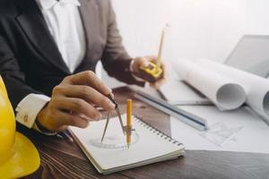 Dos colegas discutiendo el trabajo de datos y una tableta, un portátil con un proyecto arquitectónico en el sitio de construcción en un escritorio en la oficina foto