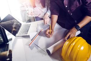 Two colleagues discussing data working and tablet, laptop with on on architectural project at construction site at desk in office photo