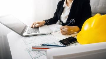 Two colleagues discussing data working and tablet, laptop with on on architectural project at construction site at desk in office photo