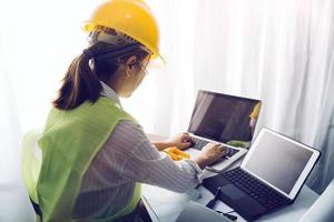 Two colleagues discussing data working and tablet, laptop with on on architectural project at construction site at desk in office photo
