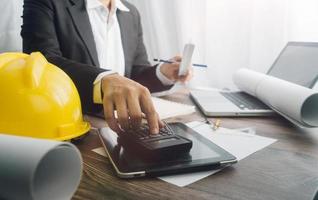 Two colleagues discussing data working and tablet, laptop with on on architectural project at construction site at desk in office photo