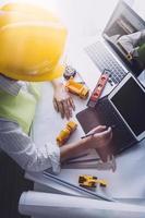 Two colleagues discussing data working and tablet, laptop with on on architectural project at construction site at desk in office photo
