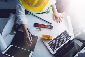 Two colleagues discussing data working and tablet, laptop with on on architectural project at construction site at desk in office photo