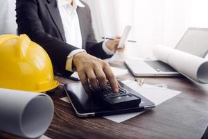 Two colleagues discussing data working and tablet, laptop with on on architectural project at construction site at desk in office photo