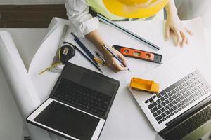 Two colleagues discussing data working and tablet, laptop with on on architectural project at construction site at desk in office photo