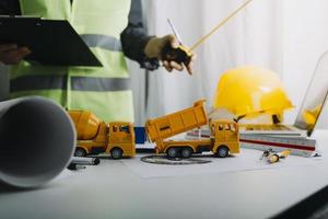 Two colleagues discussing data working and tablet, laptop with on on architectural project at construction site at desk in office photo