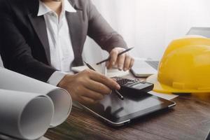 Two colleagues discussing data working and tablet, laptop with on on architectural project at construction site at desk in office photo