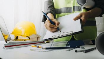 Two colleagues discussing data working and tablet, laptop with on on architectural project at construction site at desk in office photo