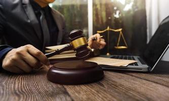 Justice and law concept.Male judge in a courtroom with the gavel, working with, computer and docking keyboard, eyeglasses, on table in morning light photo