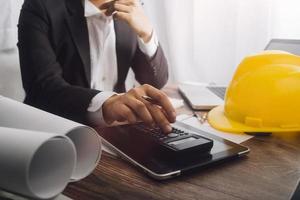 Two colleagues discussing data working and tablet, laptop with on on architectural project at construction site at desk in office photo