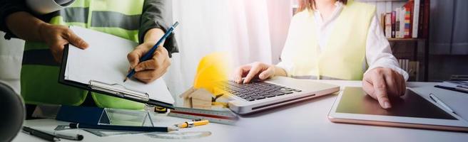 Two colleagues discussing data working and tablet, laptop with on on architectural project at construction site at desk in office photo