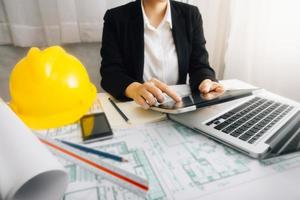 Two colleagues discussing data working and tablet, laptop with on on architectural project at construction site at desk in office photo