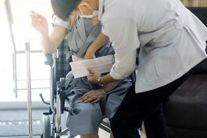 médico o enfermero cuidador con un anciano en silla de ruedas usando máscaras protectoras en casa o en un hogar de ancianos foto