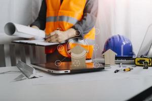 Two colleagues discussing data working and tablet, laptop with on on architectural project at construction site at desk in office photo